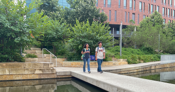 Two students walking across San Pedro Creek in front of San Pedro I.