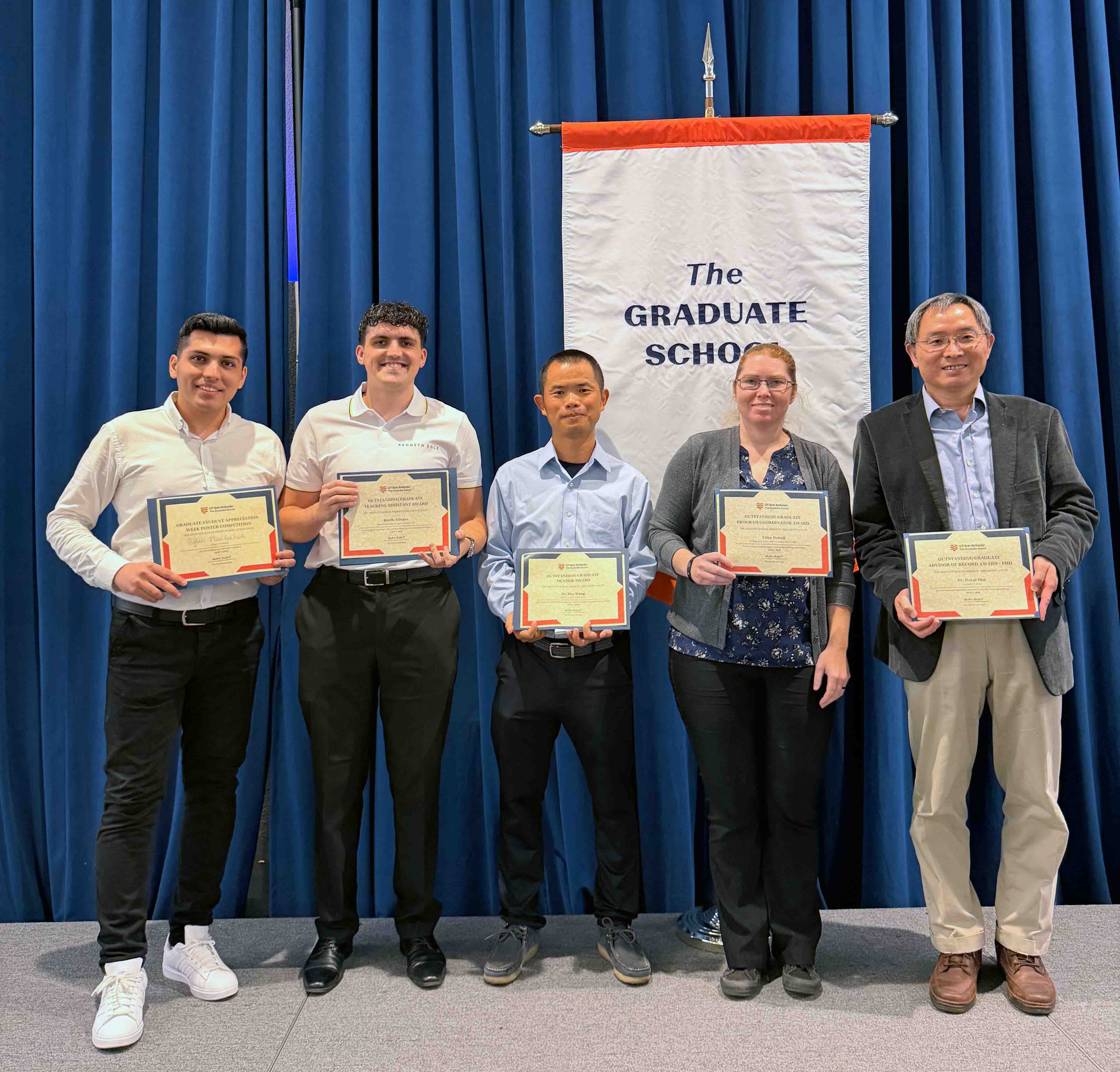 Award recipients hold their certificates in front of the Graduate School banner.